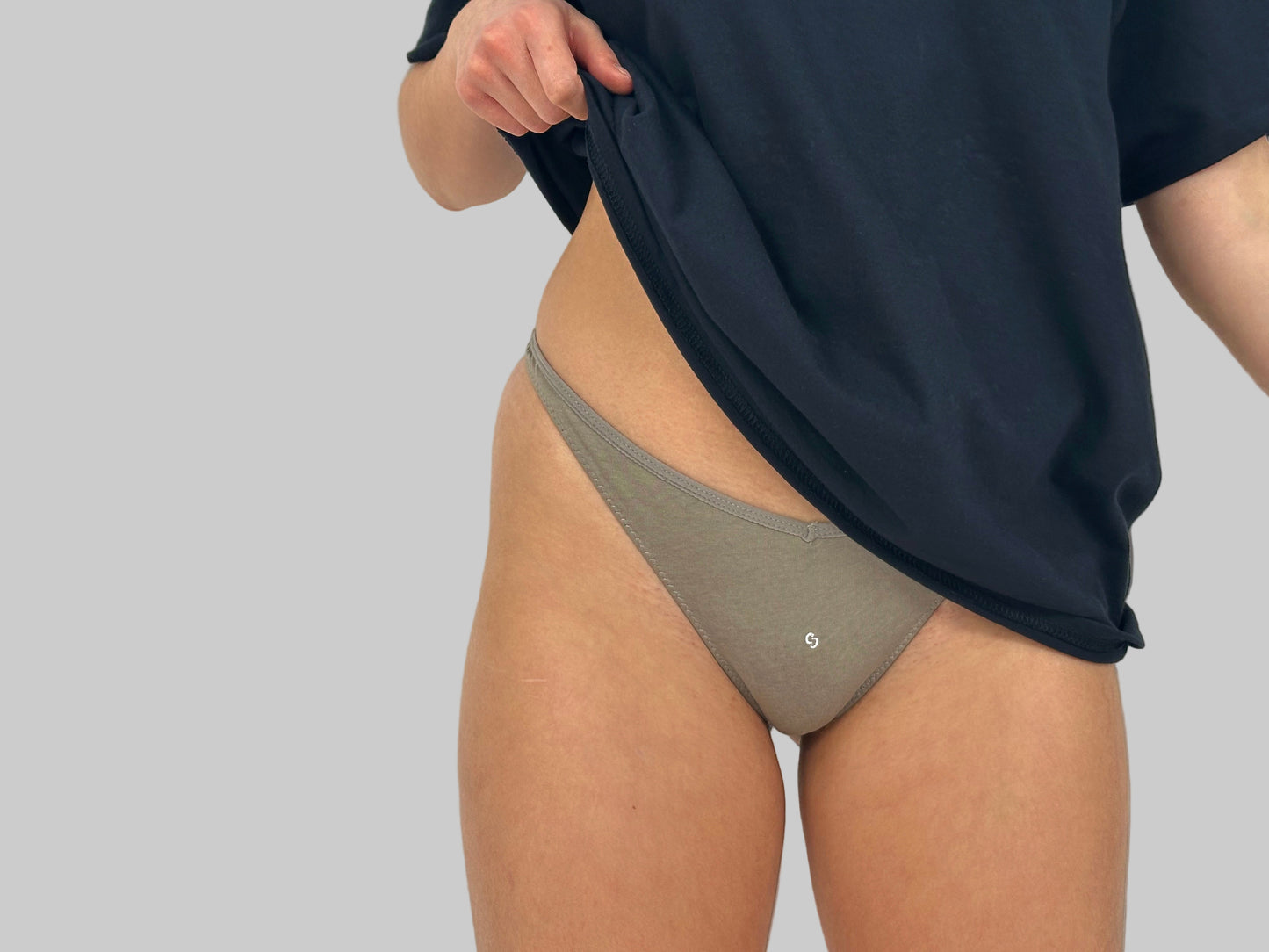 This image features a minimalist design, showcasing a pair of beige cotton thongs referred to as "Number 3 in Rain Cloud." The thong has a simple, elegant V-shape front which helps to flatter the figure by elongating the torso and accentuating the hips.