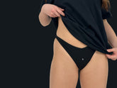 This image features a sleek, minimalist thong in a deep shade of black. The undergarment is designed with a distinctive V-shape on the front, which helps to flatter the figure by elongating the torso and accentuating the hips.