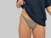 This image features a minimalist design, showcasing a pair of beige cotton thongs referred to as "Number 3 in Rain Cloud." The thong has a simple, elegant V-shape front which helps to flatter the figure by elongating the torso and accentuating the hips.